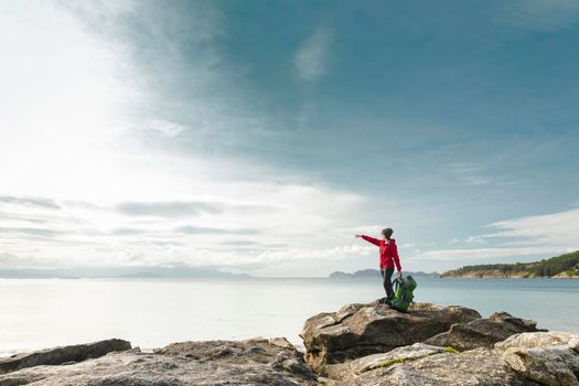 Woman with backpack enjoying and pointing to the beautiful morning view of the coast