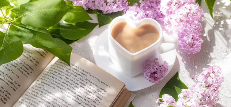 Cappuccino coffee in a cup with a book and a branch of lilac on a white background with shadows . A hot drink. Reading books. relax. Cafeteria advertising concept. Article about cappuccino. Making cappuccino. Lilac branches. Spring. Copy space