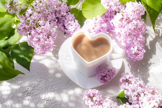 Cappuccino coffee in a cup and a branch of lilac on a white background with shadows . A hot drink. relax. The concept of cafeteria advertising. Article about cappuccino. Making cappuccino. Lilac branches. Spring. Copy space