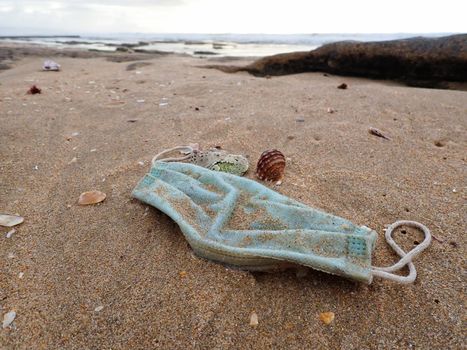 Washed-up used surgical facemask on a beach showing the pollution impact on the environment during the global pandemic, South Africa