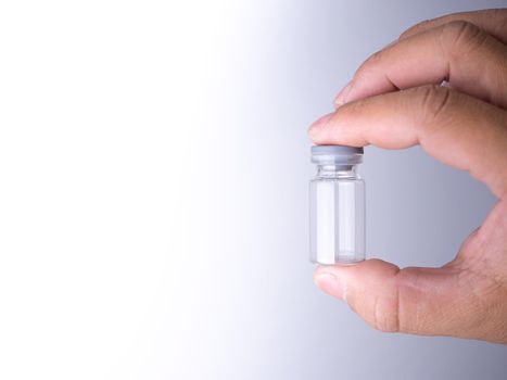 human hand holding a vaccine bottle with two fingers.