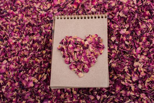 Dry rose petals form a heart shape  on a spiral notebook