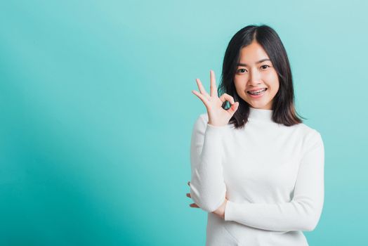 Young beautiful Asian woman smiling and showing hand the OK sign, Portrait female show finger okay gesture, studio shot isolated on a blue background