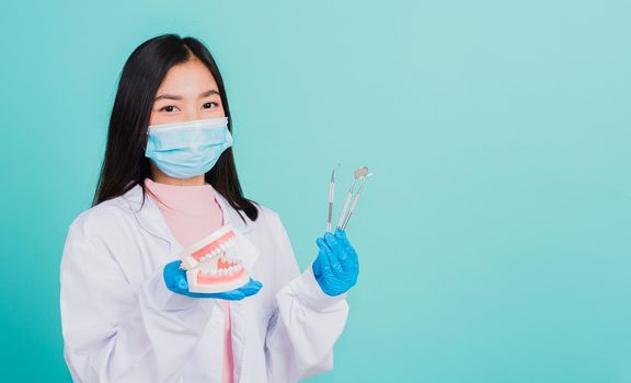 Asian beautiful woman dentist holding professional tool and model teeth denture, female doctor checking denture studio shot isolated on blue background. Dental hygiene surgery health care concept