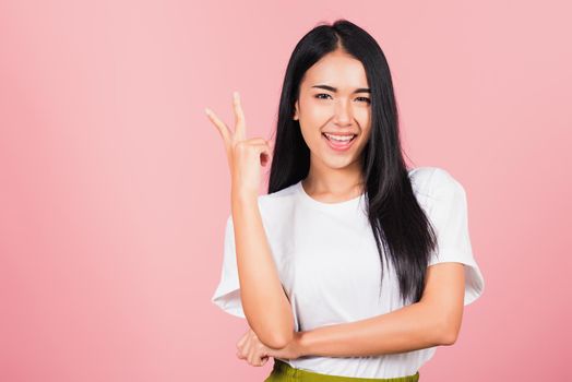 Asian happy portrait beautiful cute young woman teen smile standing show finger making v-sign victory sign gesture side away looking to camera studio shot isolated on pink background with copy space