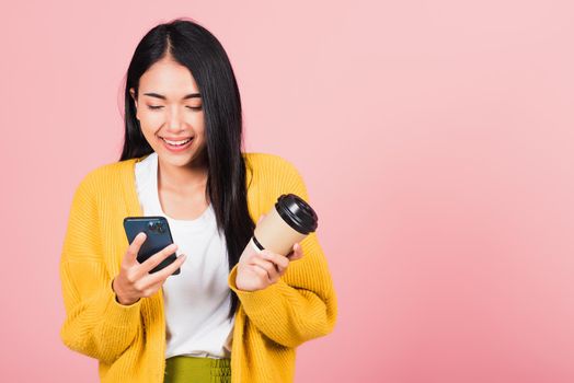 Happy Asian portrait beautiful cute young woman excited smiling holding mobile phone and coffee to go, studio shot isolated on pink background, female using smartphone with coffee cup take away