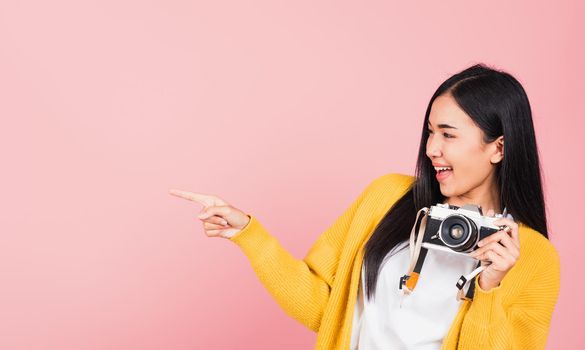 Attractive energetic happy Asian portrait beautiful cute young woman teen excited smiling holding vintage photo camera and pointing finger to side space, studio shot isolated on pink background