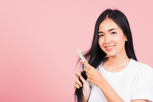 Portrait of Asian beautiful young woman smile combing her hair, happy female long healthy hair with hairbrush brushing hairs, studio shot isolated on pink background