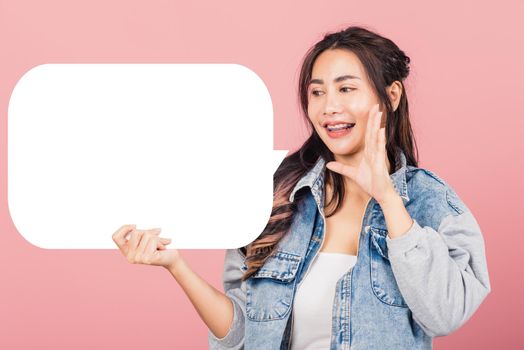 Happy Asian beautiful young woman smiling excited wear denims hand near mouth announce news and holding empty speech bubble sign, Portrait female posing idea, studio shot isolated on pink background