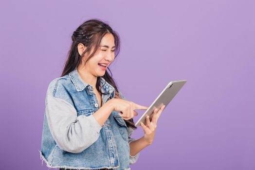 Portrait of Asian beautiful young woman smiling using tablet computer, Happy lifestyle female teen touching screen on digital tablet pc, studio shot isolated on purple background