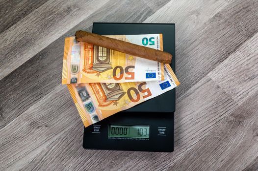 euro banknotes on top of a scale with cigar on a wooden table