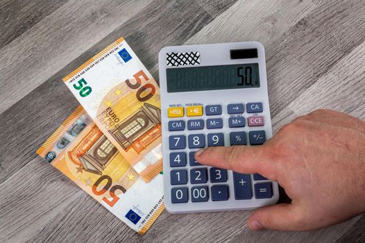 50 euro bills with calculator close up on wooden table