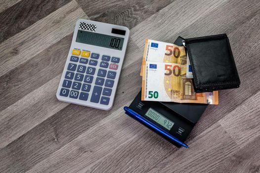 euro banknotes on top of a scale with calculator nearby on a wooden table