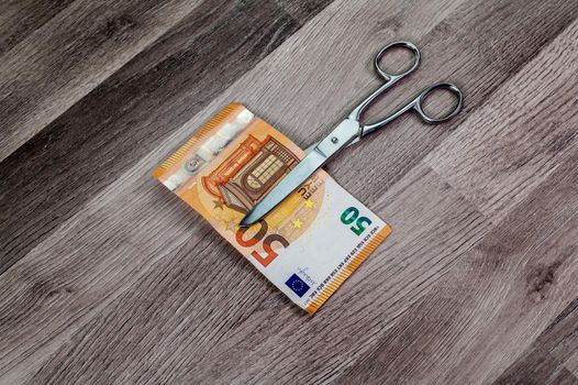 cut 50 euro banknotes with scissors on wooden table