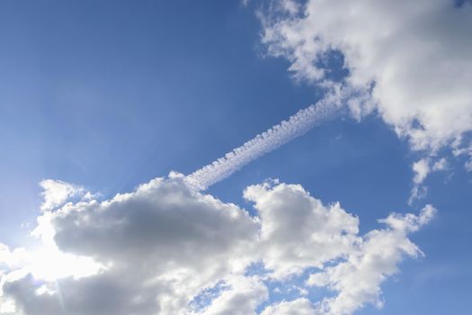 Aircraft condensation contrails in the blue sky inbetween some beautiful clouds