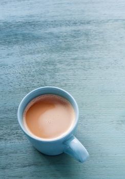 Milk coffee in a blue cup on pastel blue wooden floor