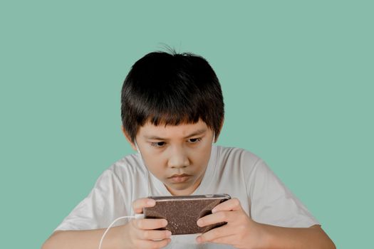 Closeup of a boy's face wearing earphones and intending to play games on his smartphone isolated on green background.