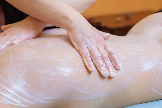 The spa master applies a scrub to the back of a young girl. Close-up.