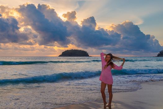 Young beautiful girl in a pink dress by the sea in the rays of the setting sun. Blonde with long hair.
