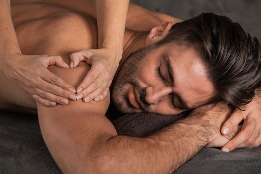 A good-looking man getting a back massage lying down at spa, Woman hand making sign heart love concept