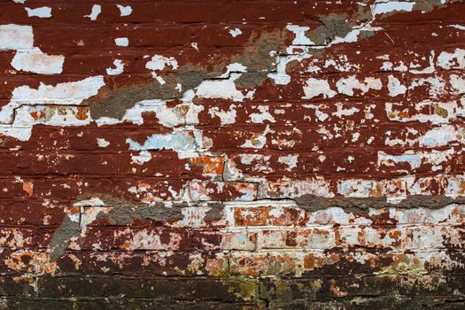 cracked shabby brick wall with old layers of brown and white paint and some mold