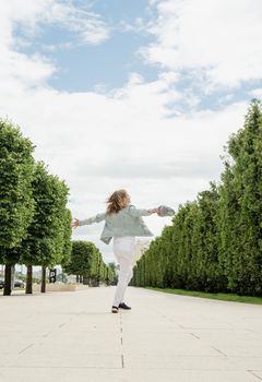 Beautiful young cheerful woman spinning around and dancing in a park. Happy woman having fun. Rear view