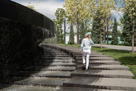 Woman in jeans clothes standing by the fountain in the park