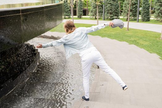 Woman in jeans clothes standing by the fountain in the park