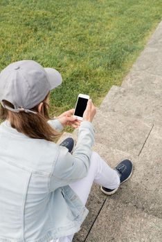 Woman in jeans clothes texting on her mobile phone, sitting on the stairs in the park. Mock up design