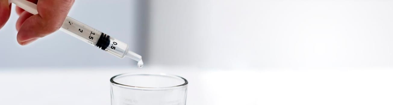 a researcher empties the liquid from a vial into a glass container to find a virus vaccine in a scientific analysis and research laboratory. Science and medical research