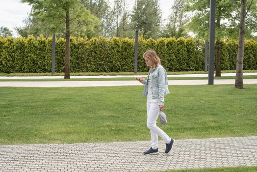 Woman in casual jeans clothes texting on her mobile phone, walking in the park