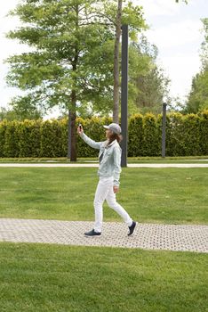 Woman in casual jeans clothes texting on her mobile phone, walking in the park