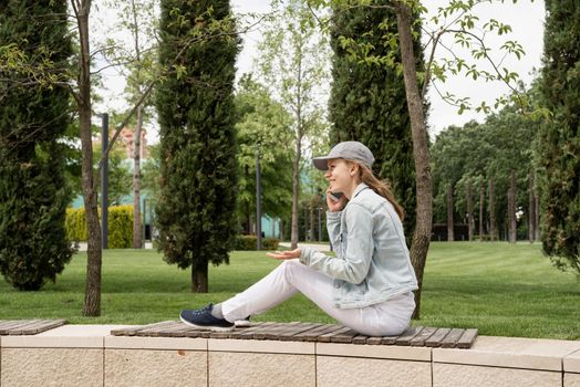 Woman sitting in the park outdoors talking on her mobile phone, sitting on the bench