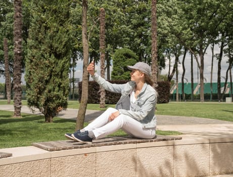 Woman sitting in the park outdoors taking selfie on her mobile phone