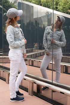 Young woman in casual jeans looking at the reflection in the mirror outdoors