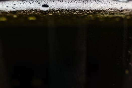 Close-up dark beer with foam and bubbles formed at the edge.