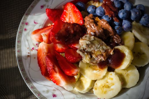 Close up shot of a healthy fruits such as banana, strawberries, blueberries on oats with milk with chocolate and hazelnut cream on top. Healthy morning breakfast concept