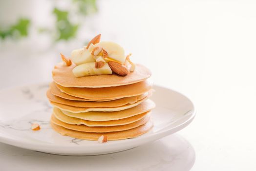 Stack of delicious pancakes with chocolate, honey, nuts and slices of banana on plate on stone background