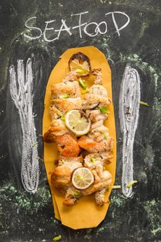 Presentation of fish skewer au gratin on chalkboard background