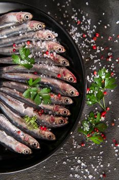 Presentation of a dish of raw anchovies on black background