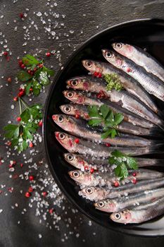 Presentation of a dish of raw anchovies on black background