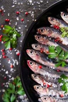 Presentation of a dish of raw anchovies on black background