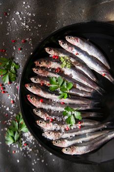 Presentation of a dish of raw anchovies on black background