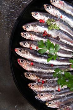 Presentation of a dish of raw anchovies on black background