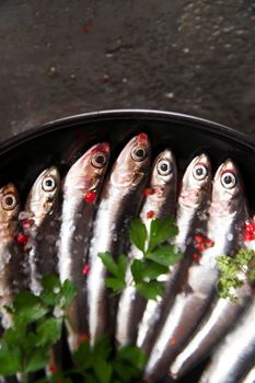 Presentation of a dish of raw anchovies on black background