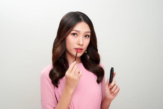 Beautiful asian woman holding red lipgloss and applying it