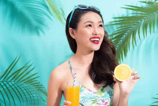 Fashion pretty woman drinks  juice from glass over colorful blue background