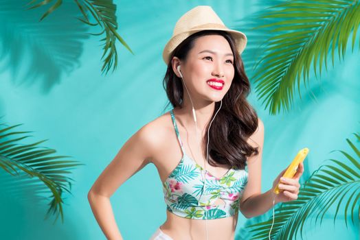 Fashion pretty asian woman listening music and smiling over bright summer background