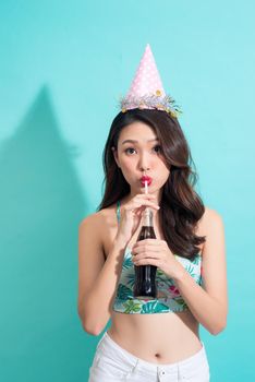 Fashion pretty woman drinks coke from bottle over colorful blue background