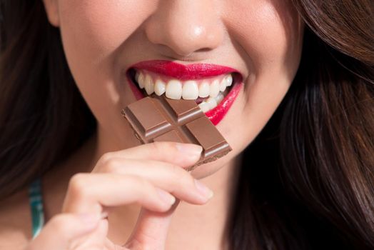 Closeup of a woman with red lipstick eats chocolate